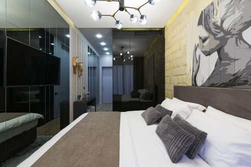 Free Modern bedroom interior with cushions on bed reflecting on wall against artwork illuminated by chandelier Stock Photo