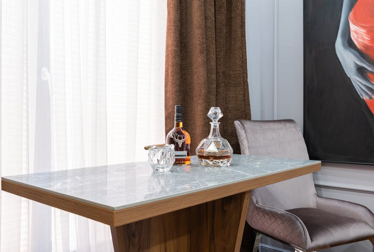 Whiskey In Bottle Between Glass And Carafe On Table