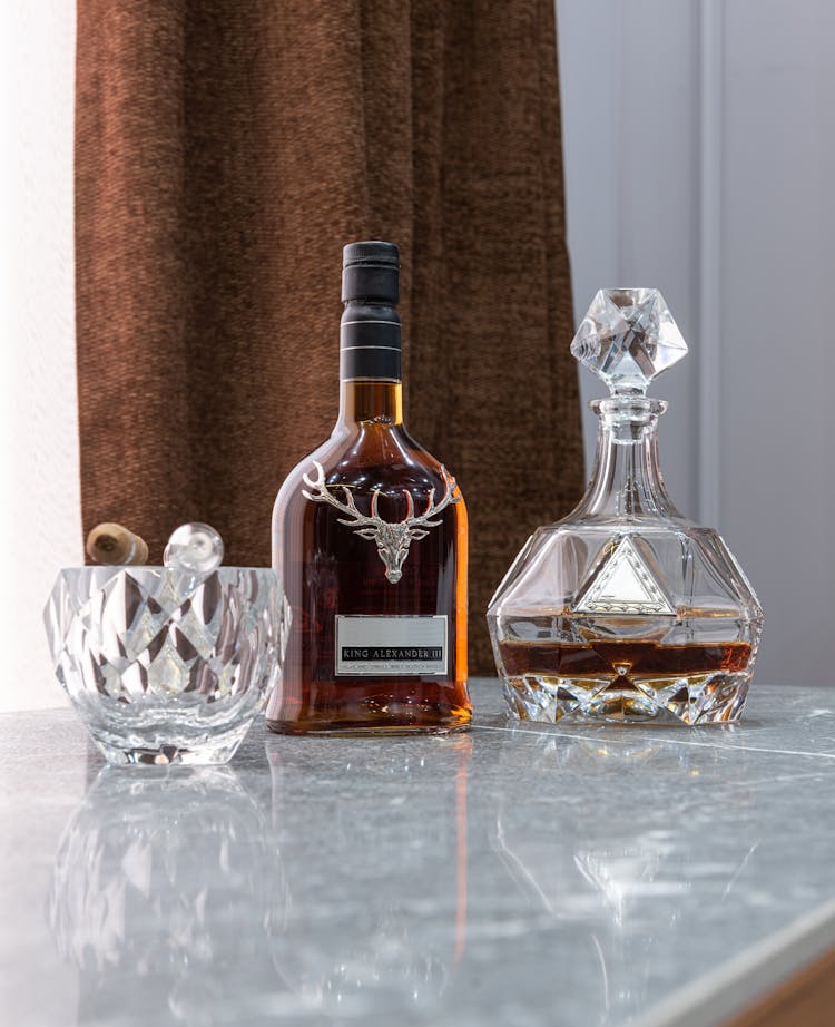 Bottle Of Whiskey Between Decanter And Ornamental Glass With Cigar