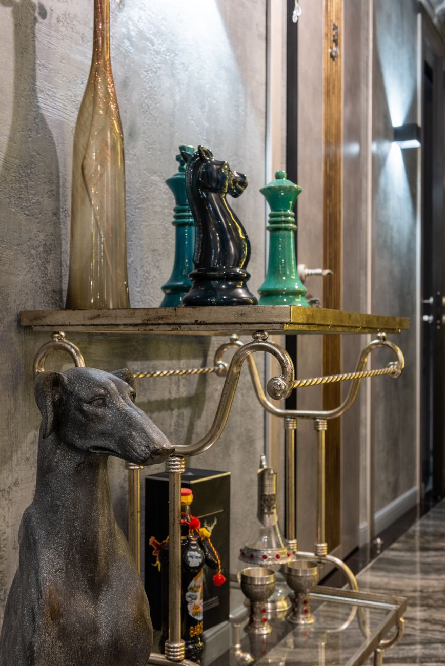 Decorative dog against table with chess pieces under bottles and chalices at home illuminated by artificial light