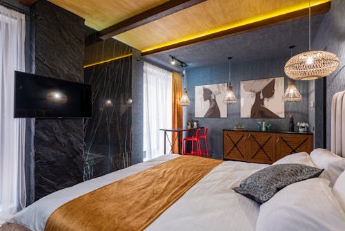 Soft bed against LED television and paintings on wall illuminated by hanging lamps in house