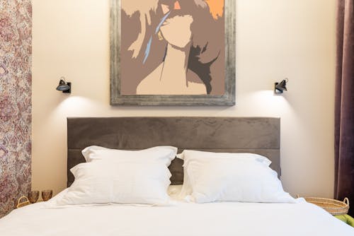 Free Soft pillows on bed against artwork on wall with shiny lamps and ornament in house Stock Photo