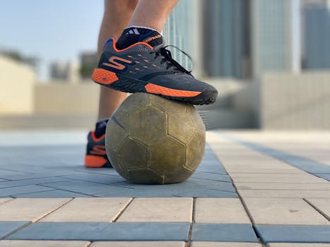 A person wearing sports shoes stepping on a soccer ball outside.