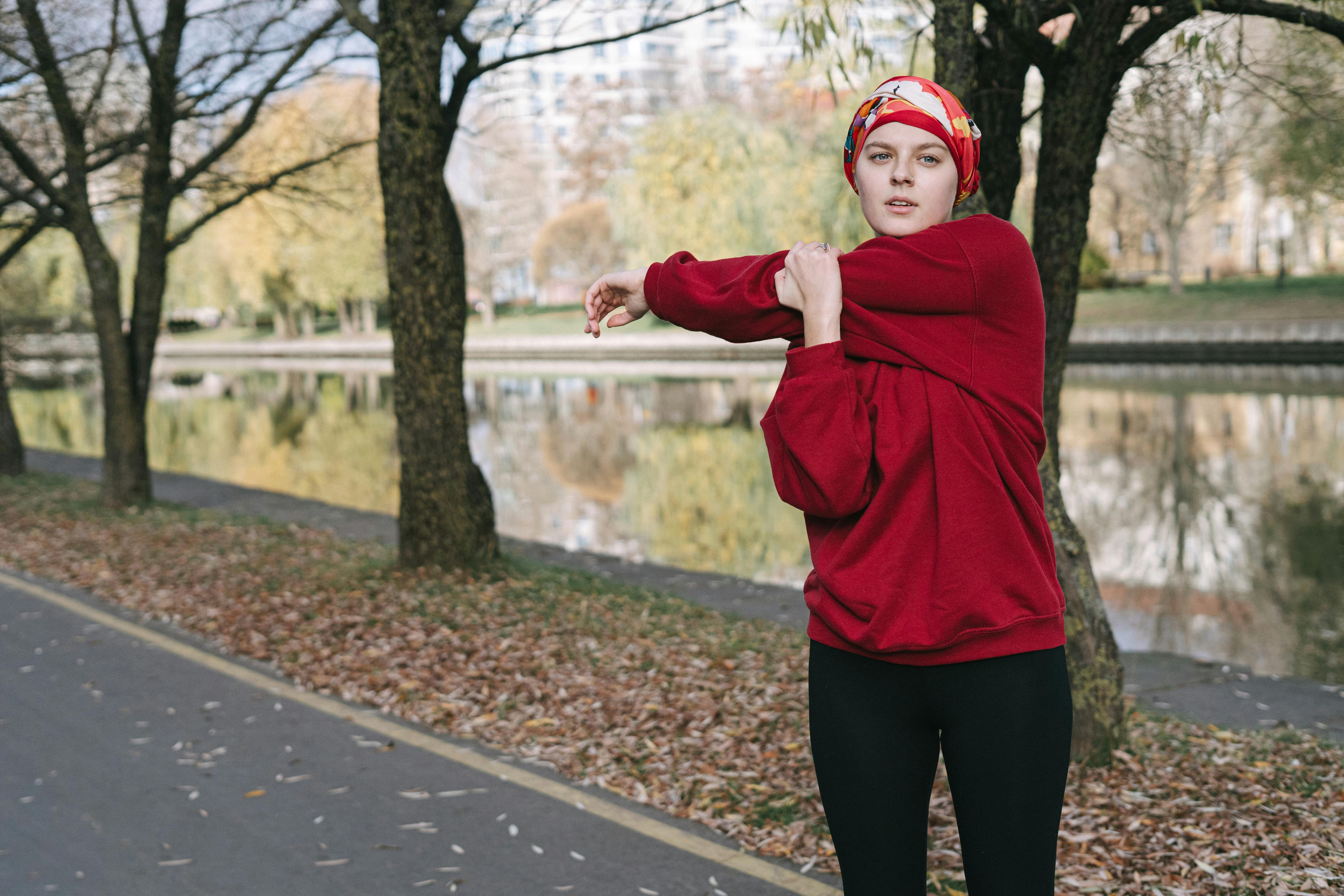 Woman in red sweater stretching by a riverside path during fall.