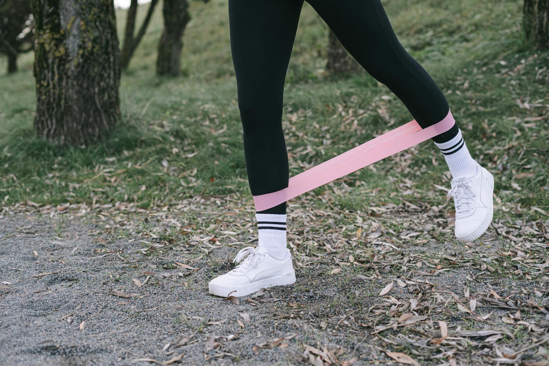 A Person in Black Leggings Working Out with a Pink Resistance Band