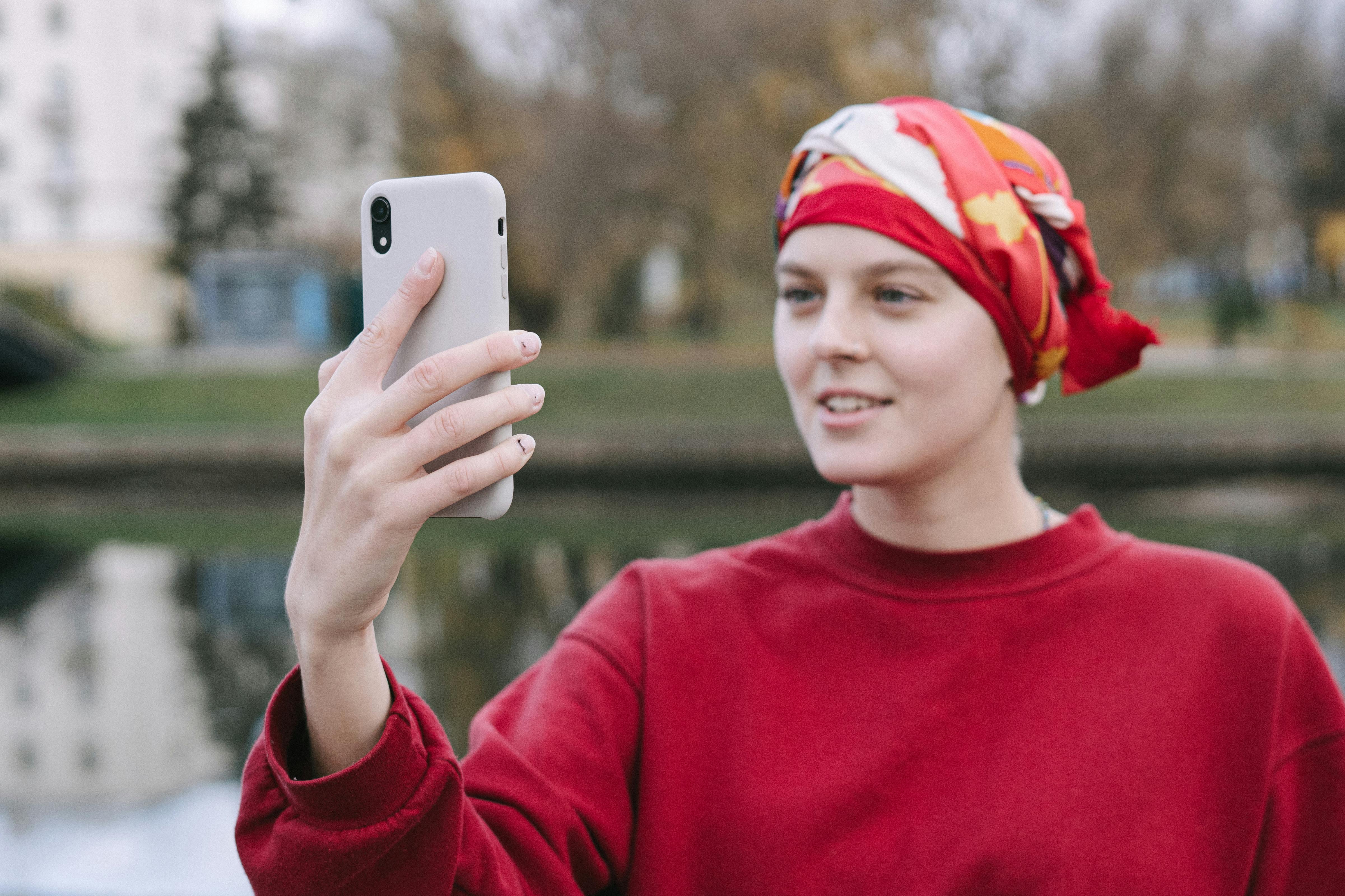 Woman in red headscarf making a video call outdoors during fall season.
