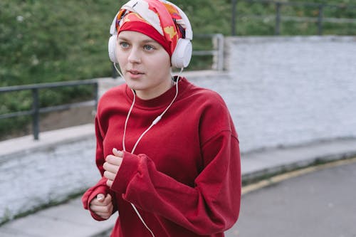 Free Close-Up Shot of a Woman in Red Pullover Jogging while Listening to Music Stock Photo
