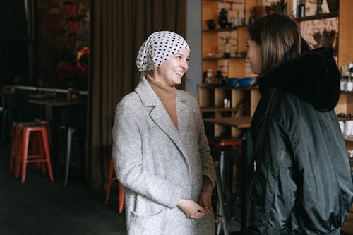 Free A Woman in Gray Coat Smiling while Looking at Her Friend while Having Conversation Stock Photo