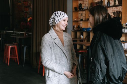 Free Two women in stylish winter coats enjoying a friendly conversation in a cozy café. Stock Photo