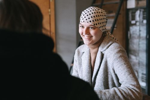 Free A woman wearing a headscarf and gray coat smiling indoors, embodying warmth and resilience. Stock Photo