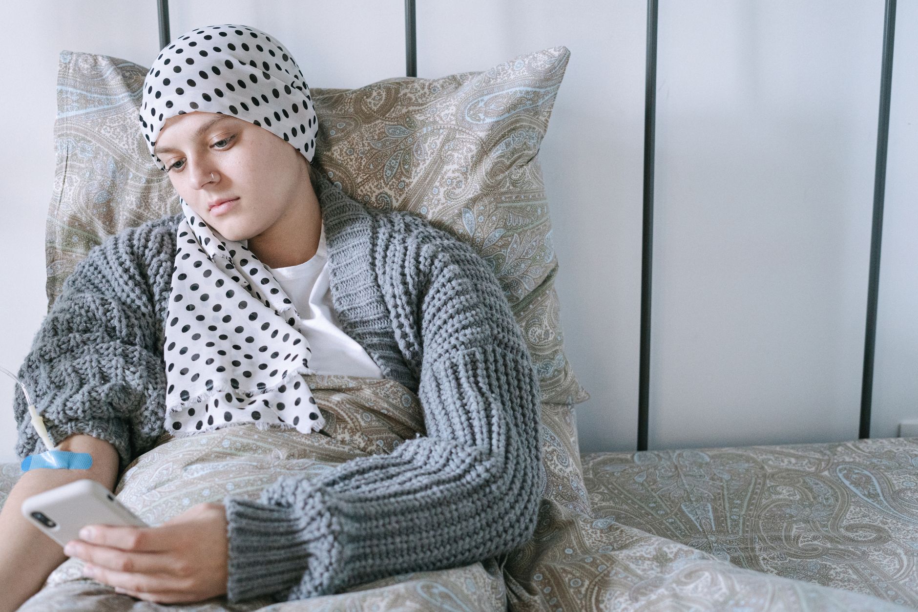 유병자 보험, 현명하게 가입하는 5가지 핵심 가이드 2 Woman resting in bed wearing a scarf, using her phone during cancer treatment.
