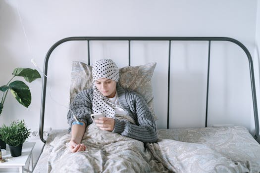 A woman undergoing chemotherapy checks her smartphone in a hospital bed, symbolizing hope and recovery.
