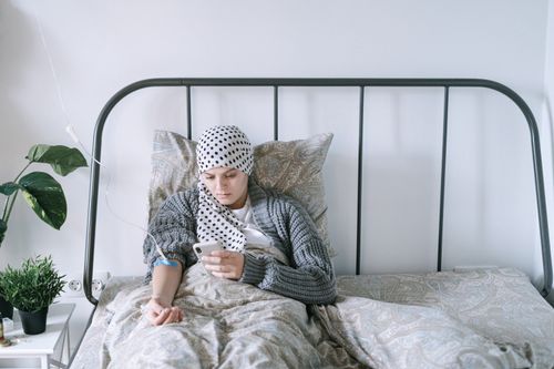 Free A woman undergoing chemotherapy checks her smartphone in a hospital bed, symbolizing hope and recovery. Stock Photo