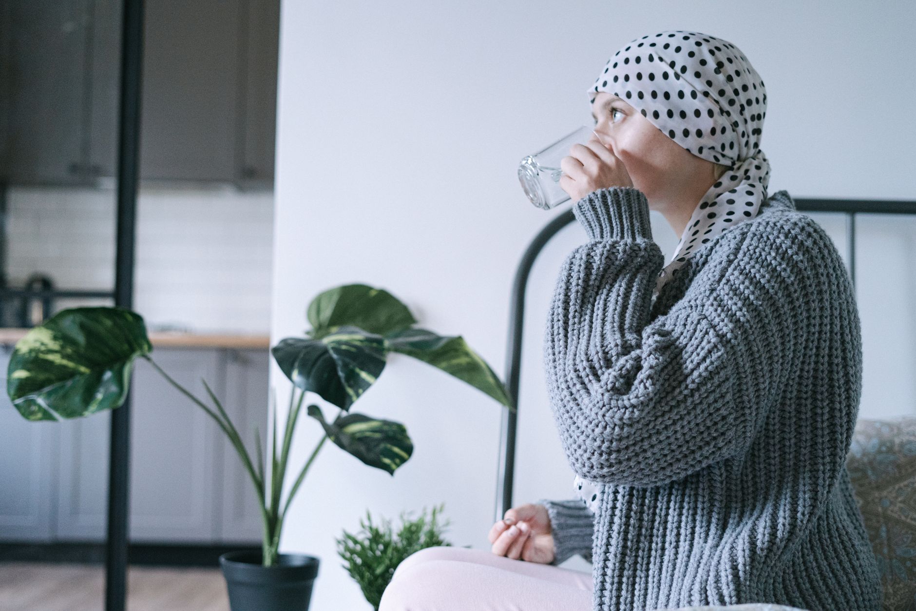 A woman wearing a headscarf drinks water indoors, promoting recovery and wellness.