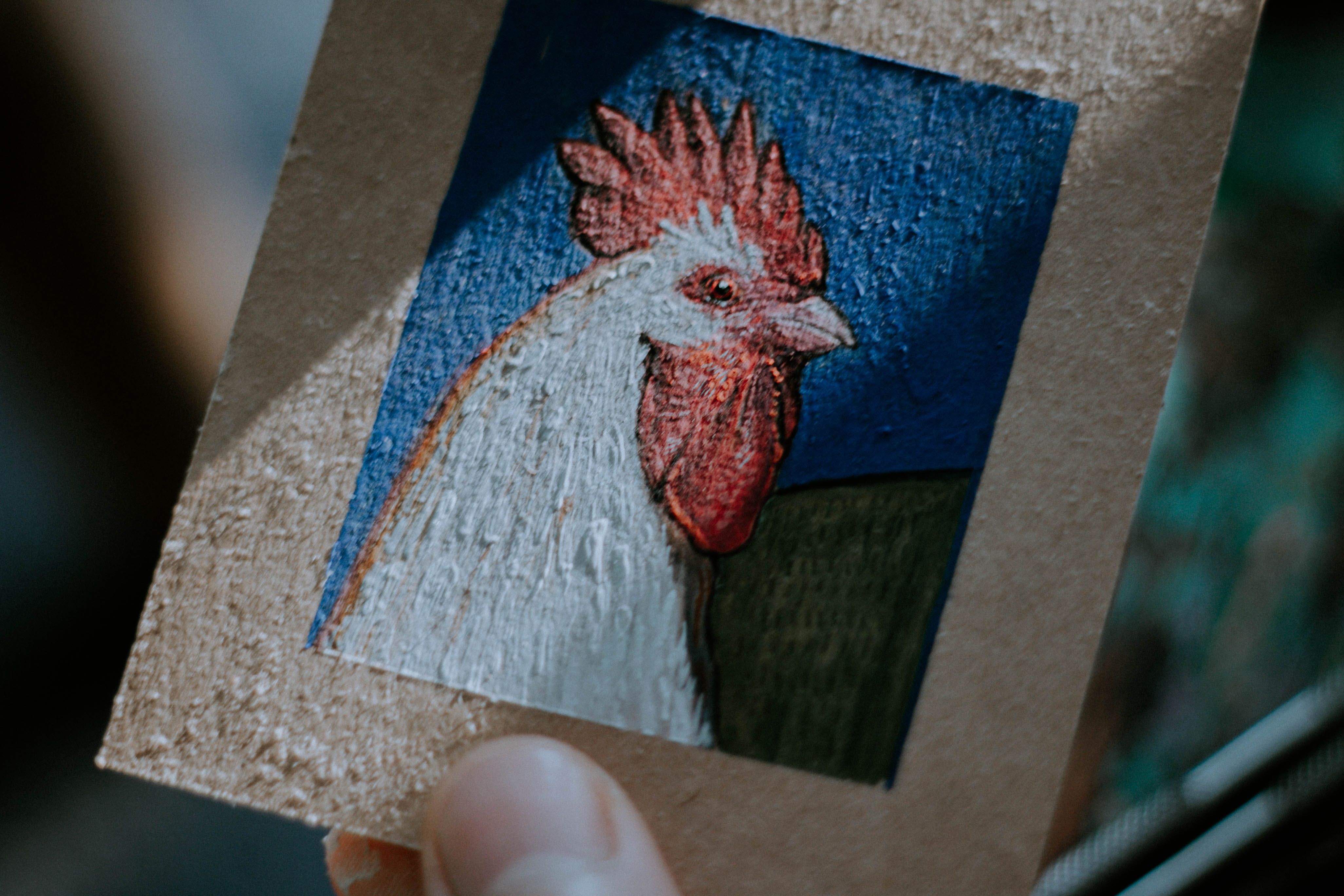 Captivating close-up of an acrylic painting featuring a rooster on a cardboard canvas.