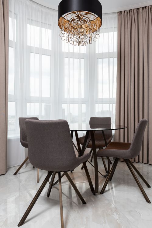 Free Chairs and table on floor under decorative chandelier against pleated curtains in contemporary house in daylight Stock Photo