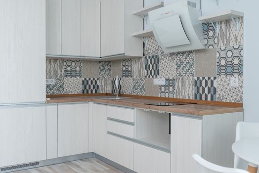 Interior of contemporary kitchen with white cabinets and wooden counter near ornamental tile on wall and modern appliances in apartment