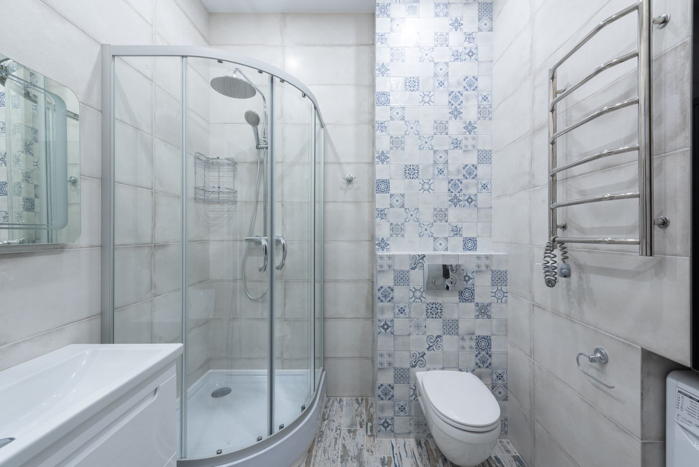 Compact bright bathroom with a curved glass shower enclosure, tiled walls, patterned accent tiles, wall-hung toilet and heated towel rail.