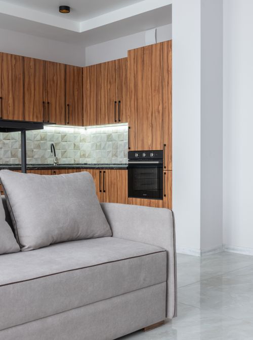 Free Interior of contemporary spacious light room with kitchen counter with modern oven near wooden cabinets and comfortable sofa at home Stock Photo