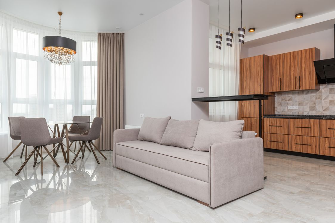 Free Interior of modern flat with kitchen counter with wooden cabinets placed near sofa bar counter and table with chairs at home Stock Photo