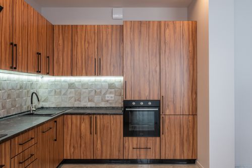 Free Interior of kitchen with wooden cupboards and contemporary black oven near marble counter with sink and tiled wall in light apartment Stock Photo