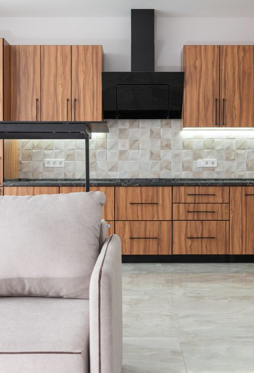 Free Interior of modern kitchen with wooden cupboards and black exhaust hood placed in room with tiled wall and comfortable sofa Stock Photo