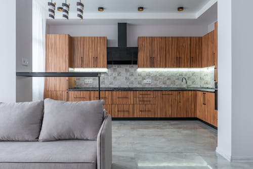 Modern kitchen with wooden cabinets and black exhaust placed near bar counter and soft sofa in light spacious room at home