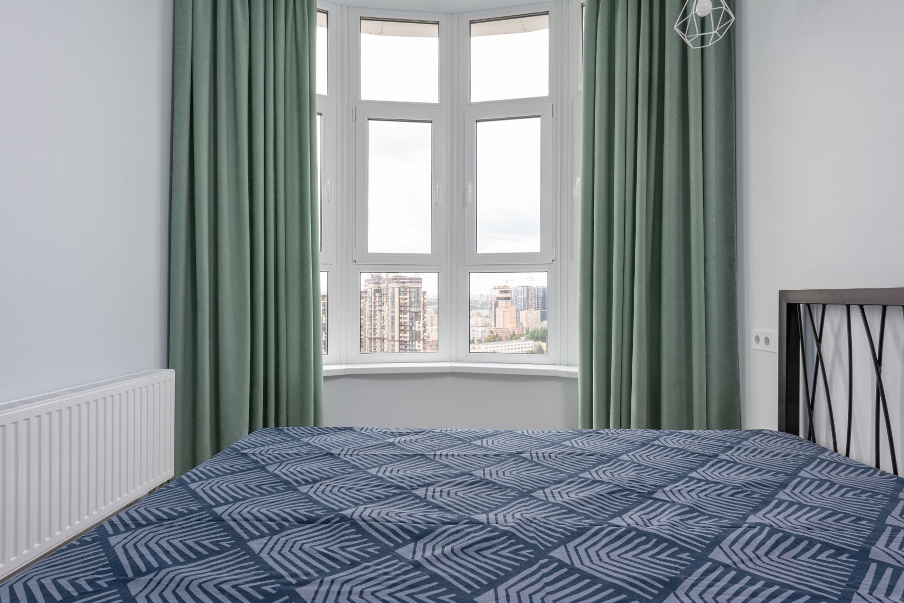 Small bedroom with a bed beside a large window, green curtains and a visible wall heater