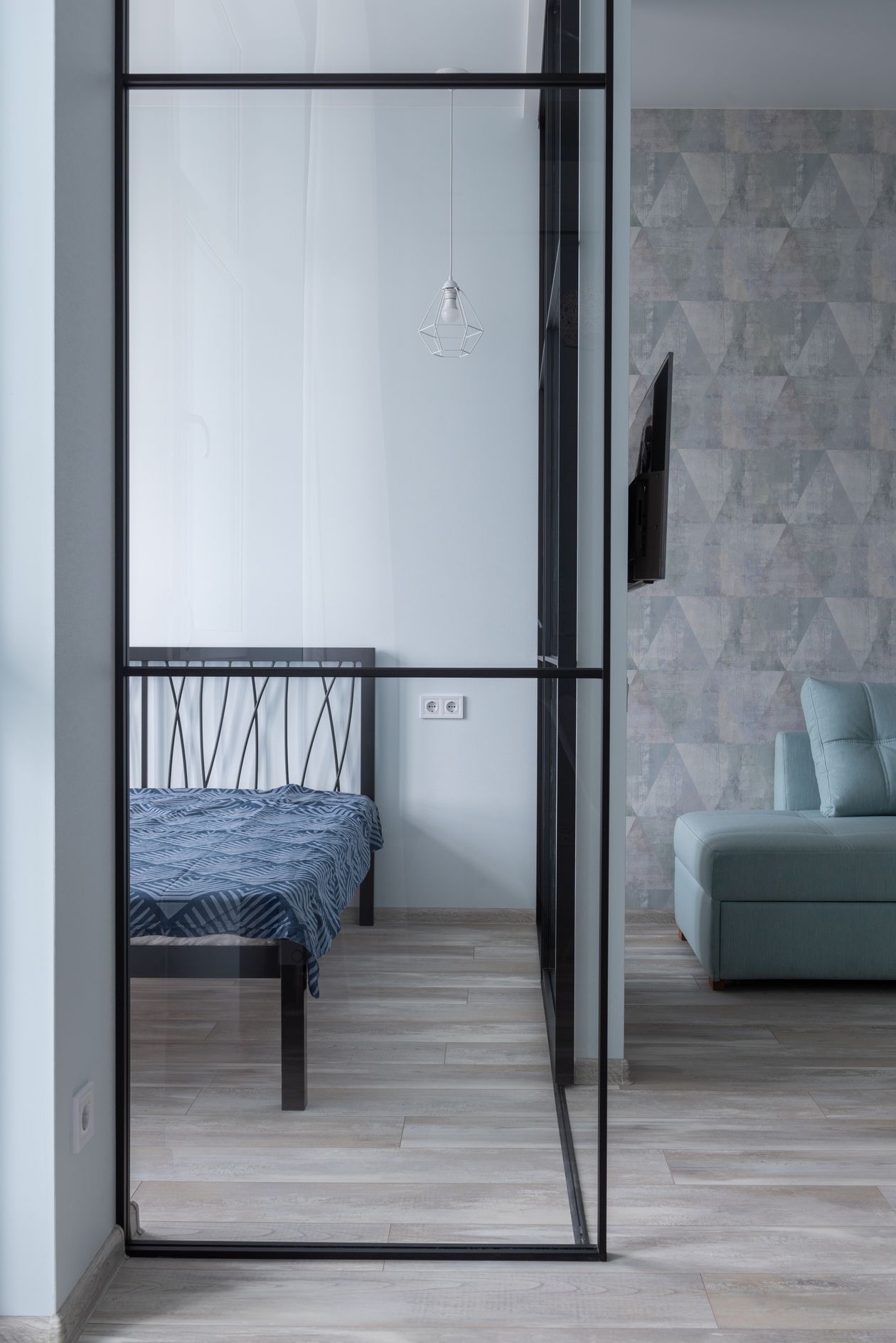 A black-framed glass partition with sheer cream curtains separating a bedroom from a vanity area