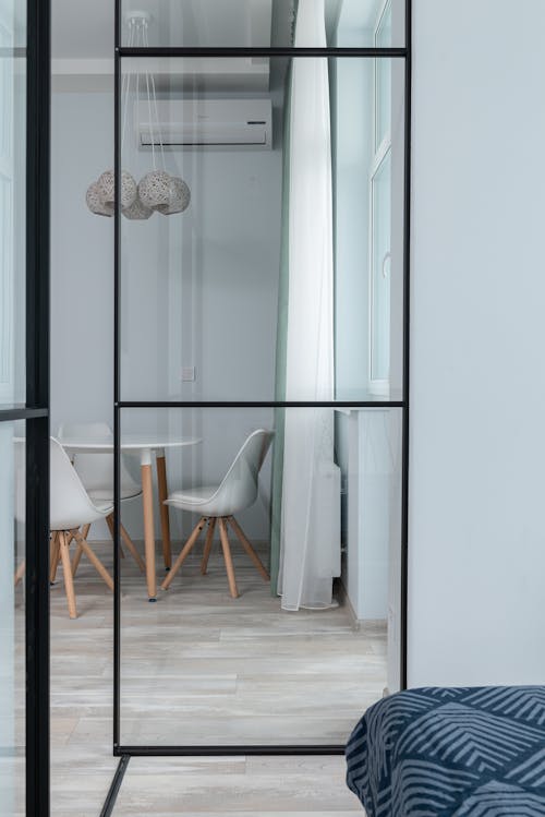 Free View of round white table with chairs through glass wall of bedroom with blanket on bed placed in modern apartment Stock Photo