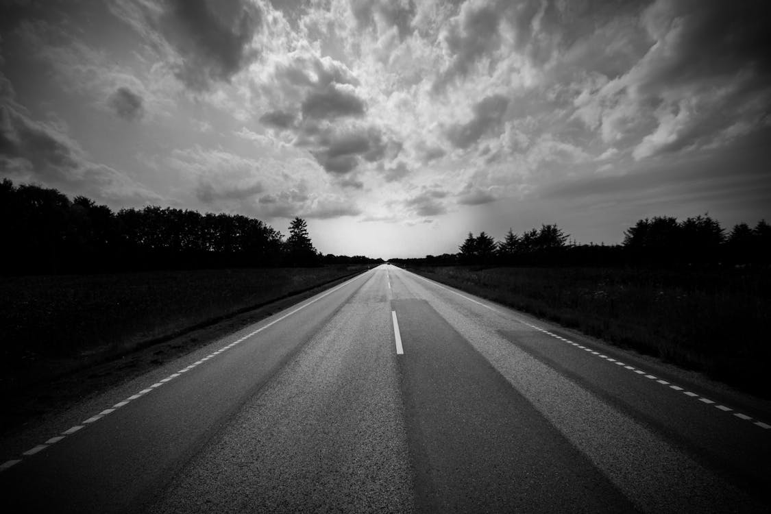 Grayscale Photo of Winding Road Under A Cloudy Sky