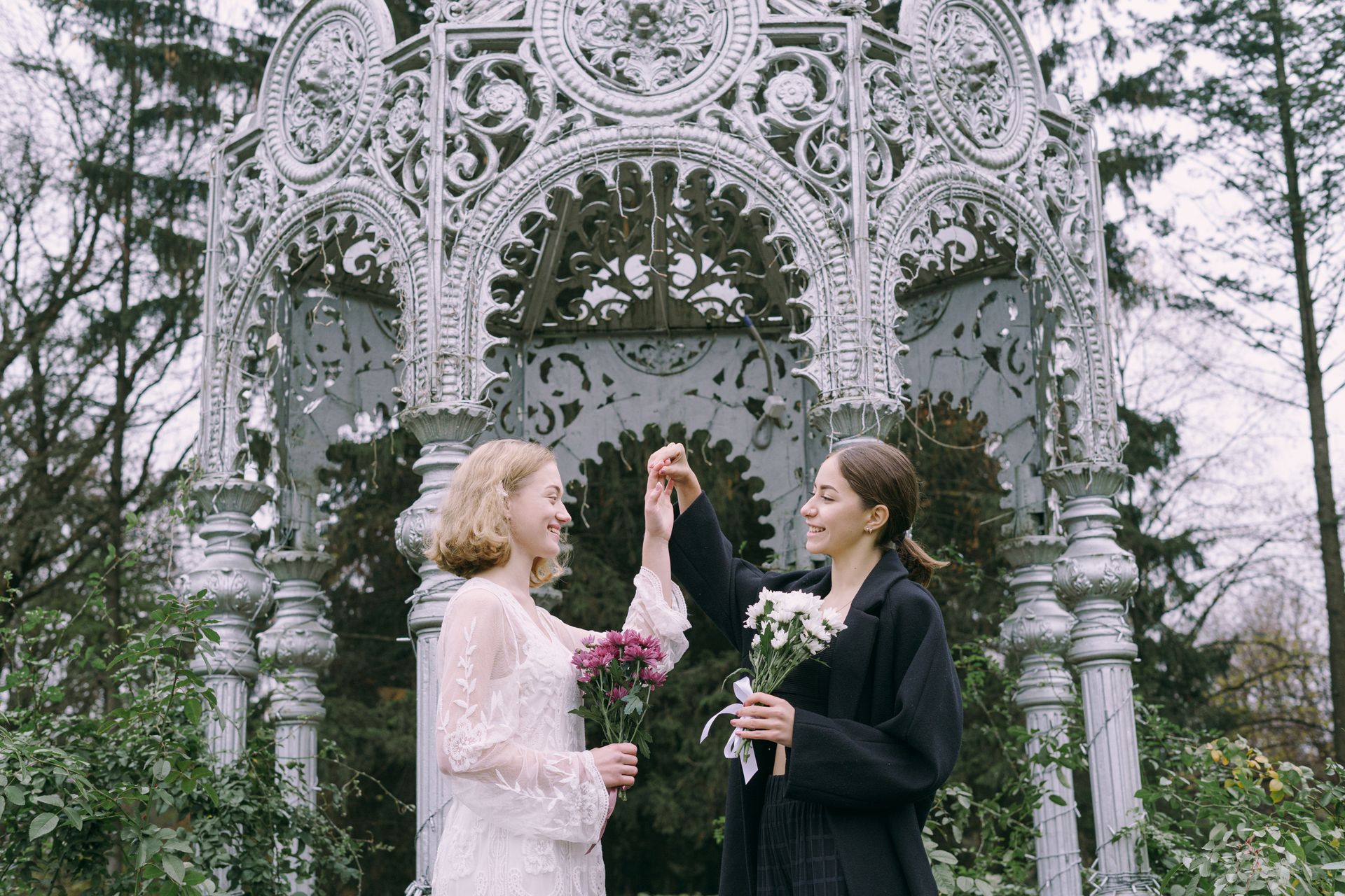 A joyful couple celebrating in a vintage gazebo with bouquets, capturing love and happiness outdoors.