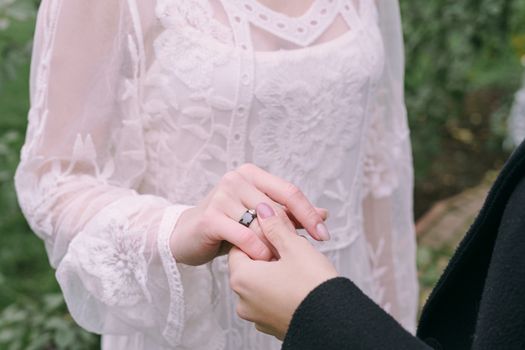 Womans Hand in Black Long Sleeve Holding Hand of Woman in White Laced Dress with Black Ring
