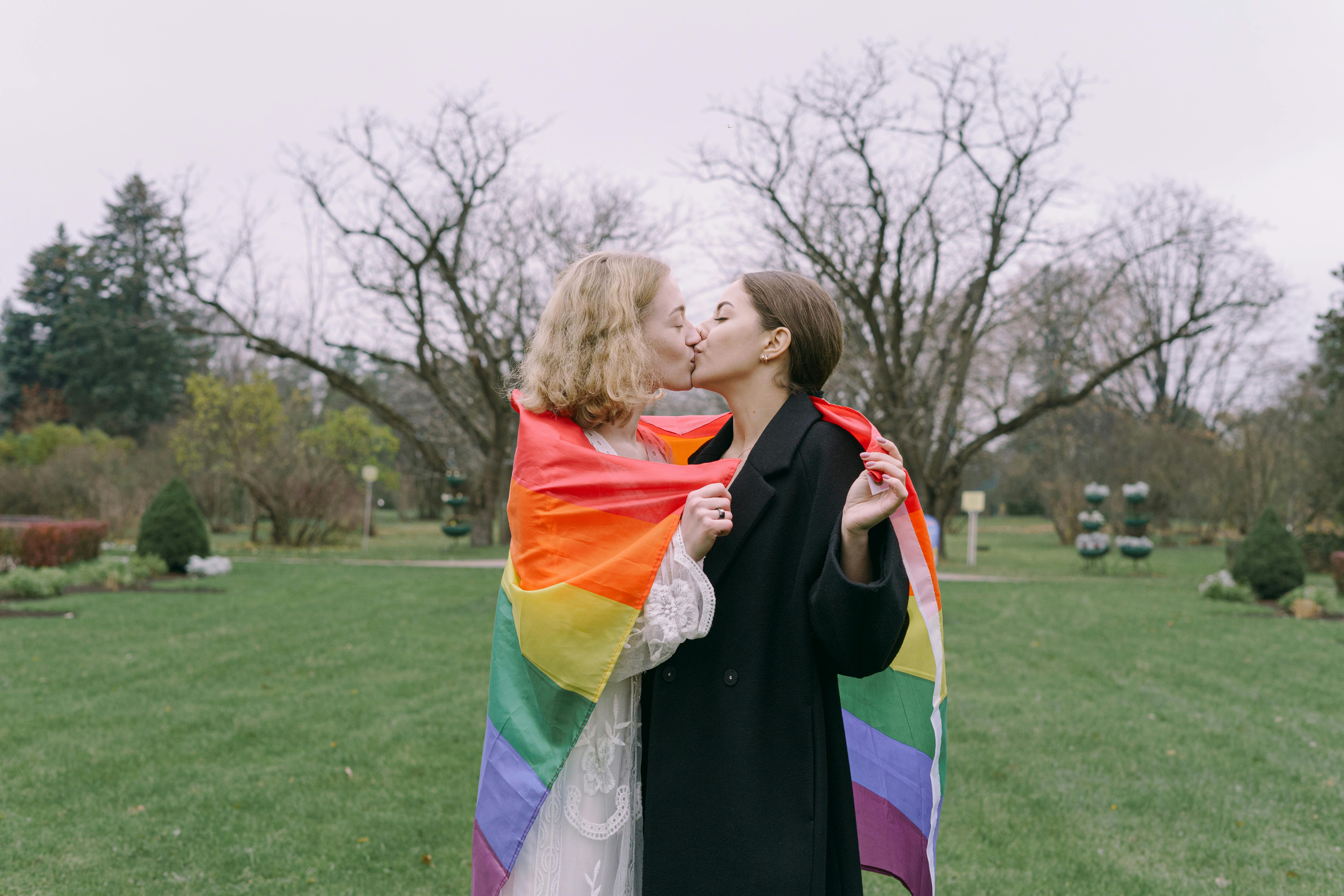 same sex couple kissing while holding gay pride flag