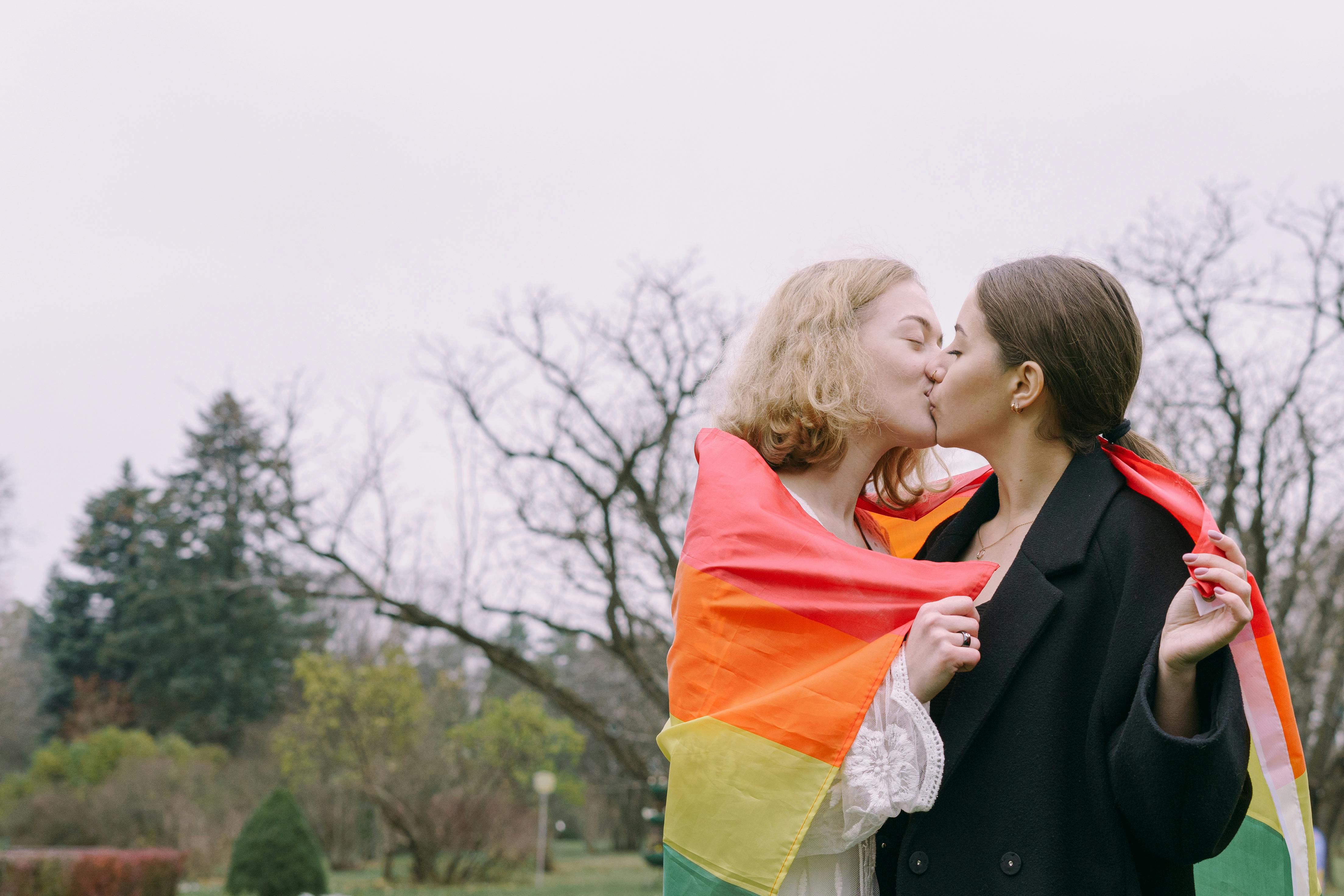 same sex couple kissing while holding gay pride flag