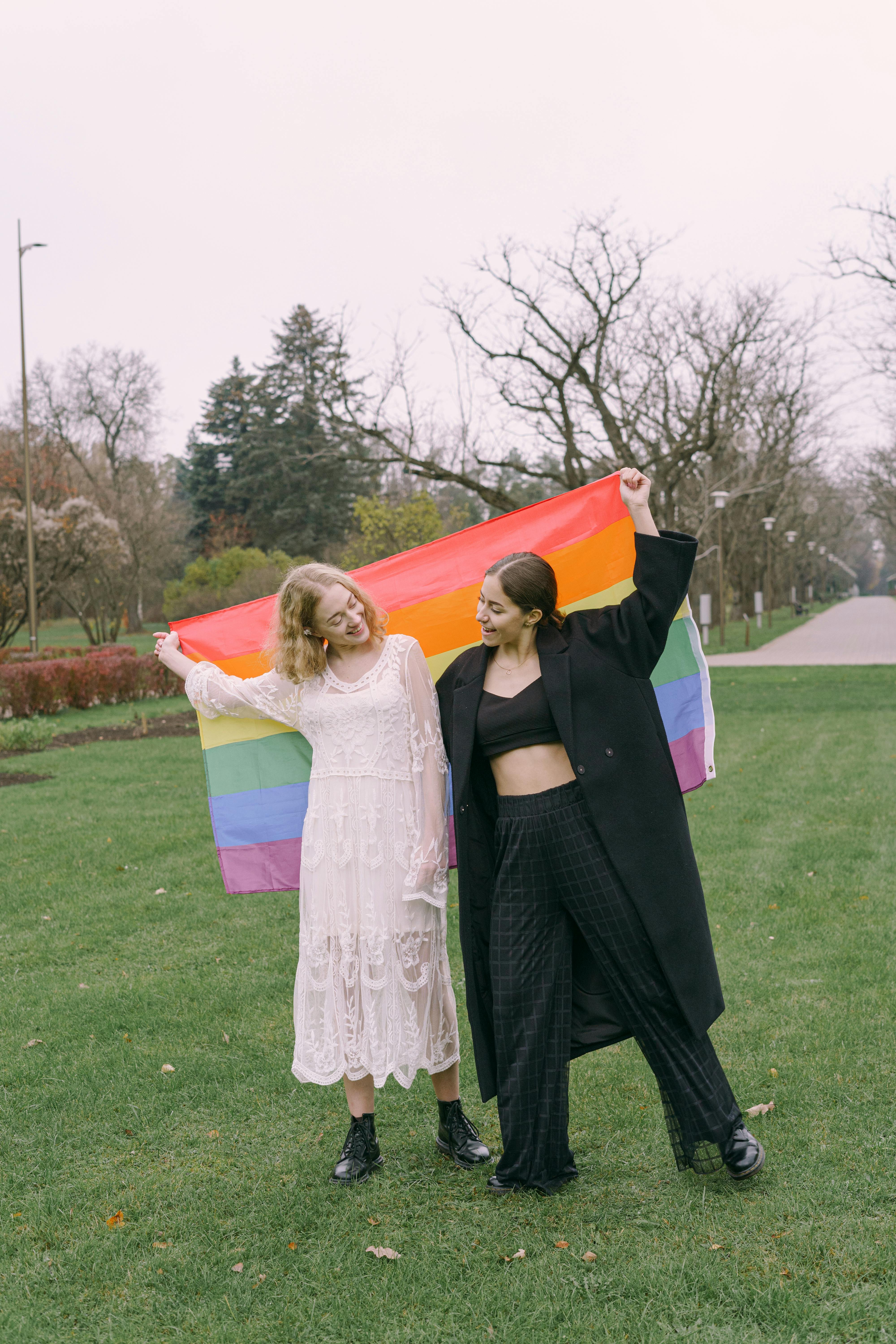 couple standing on green grass holding rainbow flag