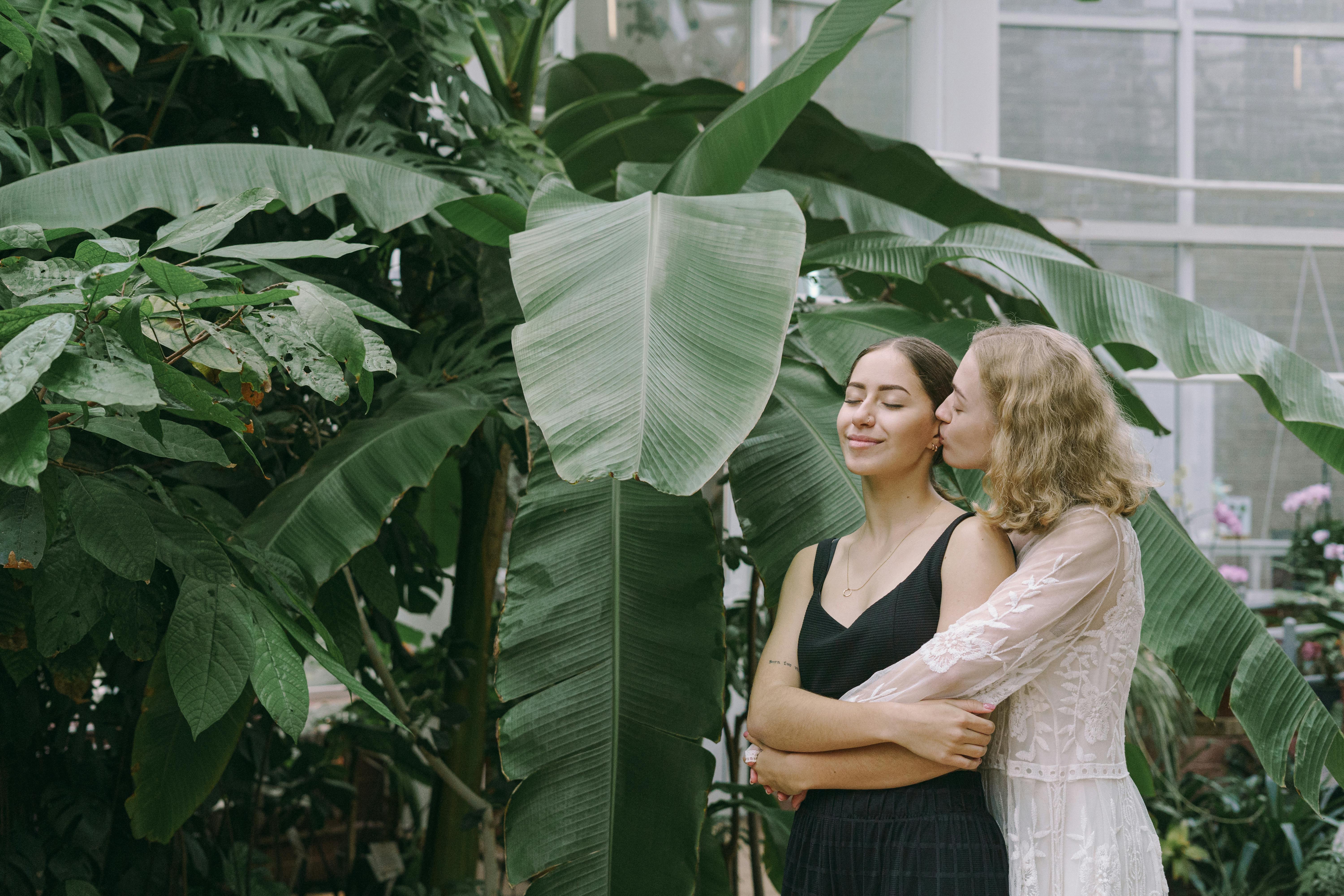 a same sex couple embracing each other while standing near the green plants