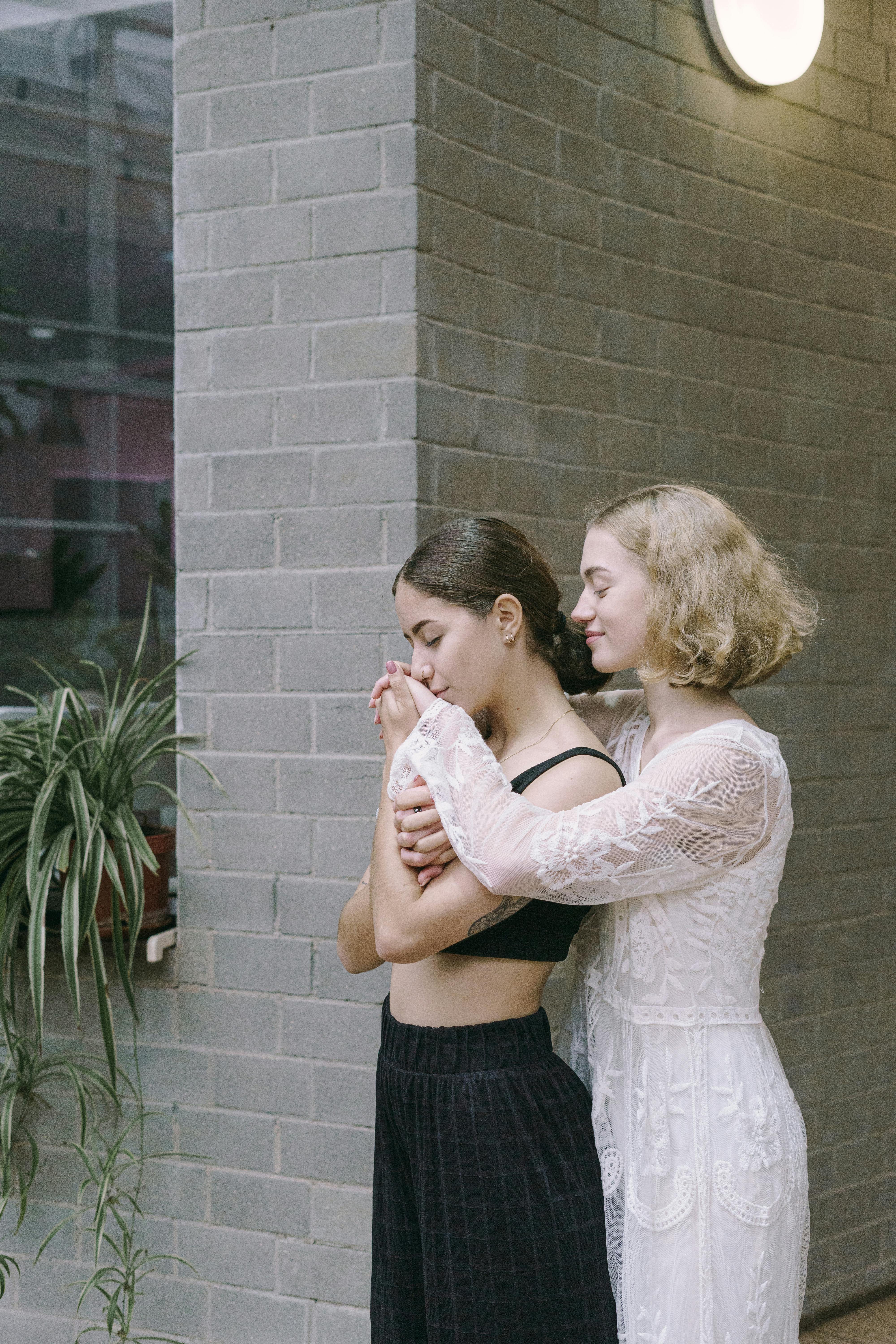 a couple embracing each other while standing near the brick wall