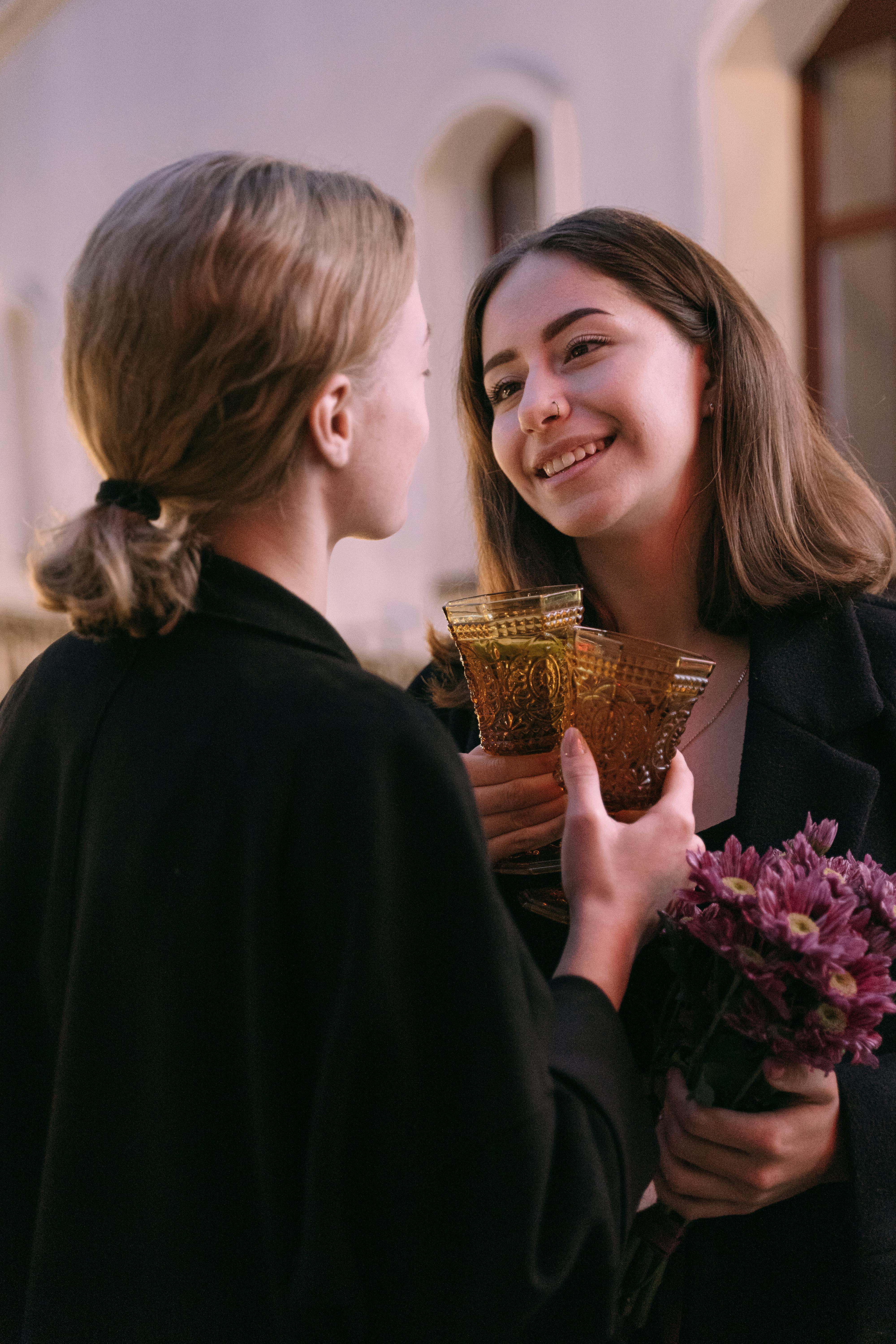 a same sex couple facing each other while holding a wine glasses