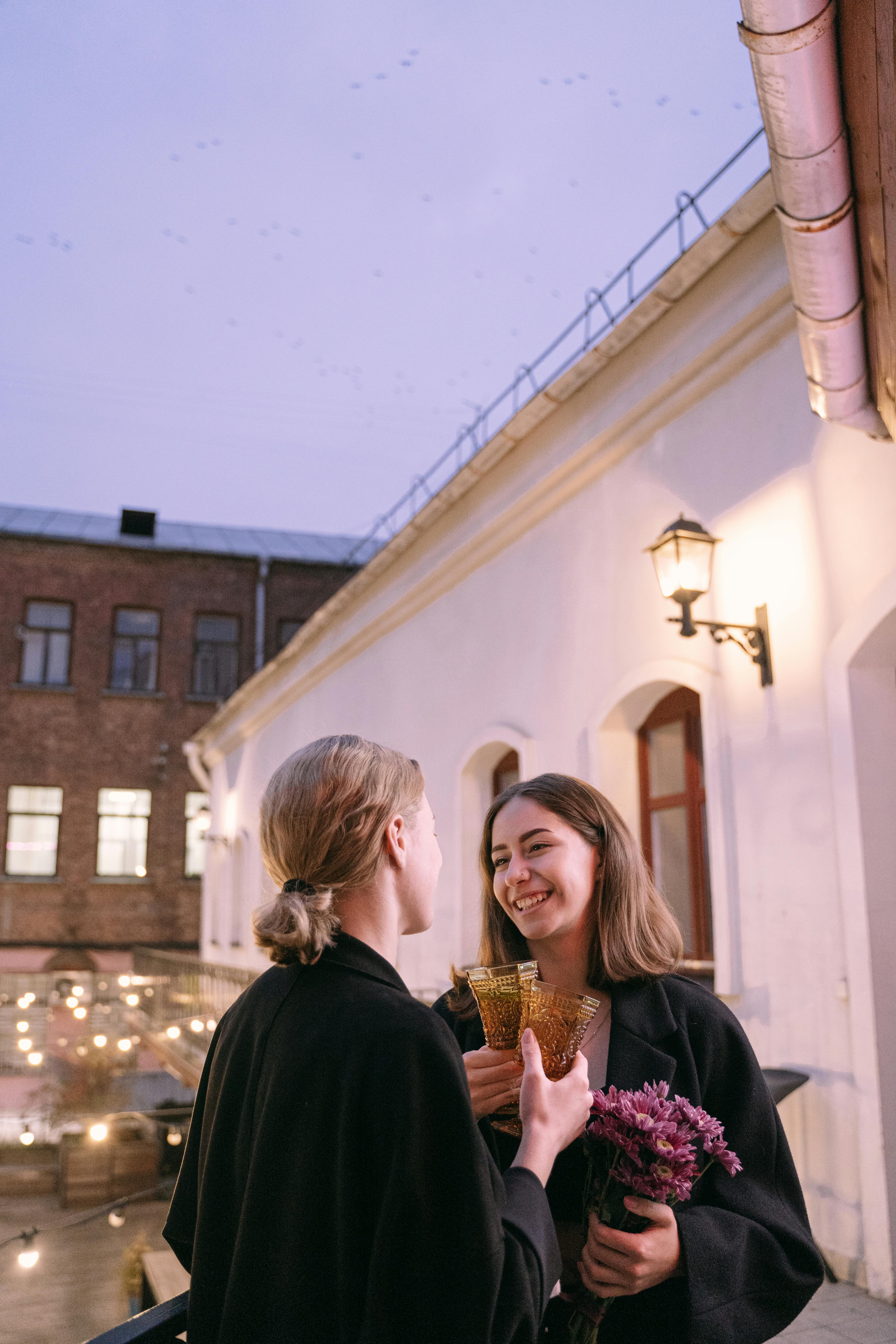 a same sex couple having conversation at the balcony while holding drinks