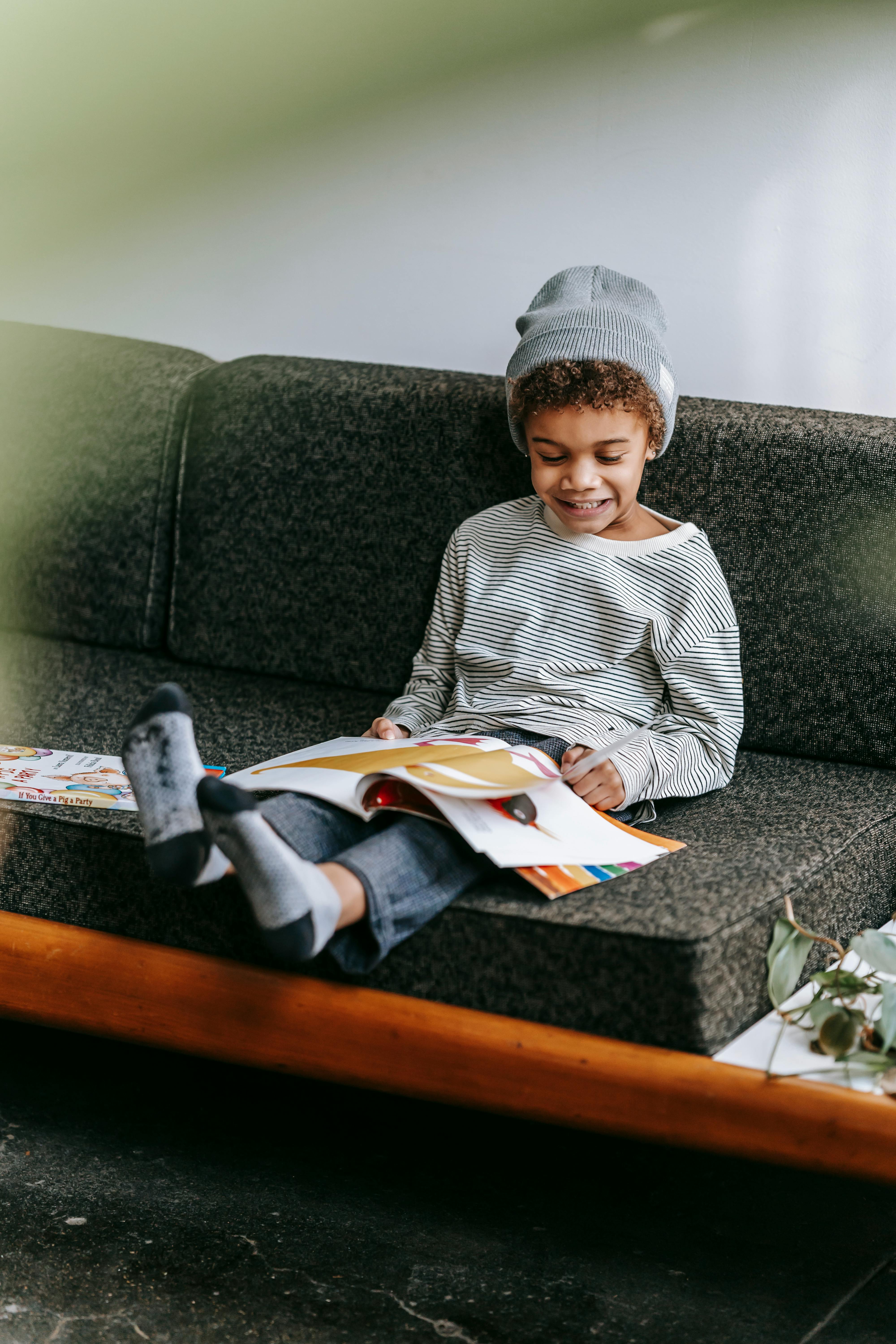 happy adorable black boy reading magazine on sofa