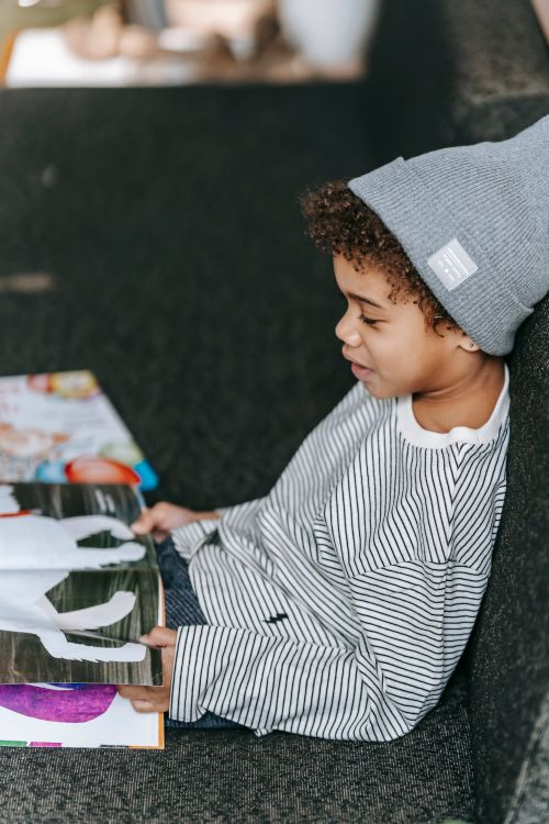 Free Side view of adorable African American boy in casual trendy outfit watching pictures in book with fairytale Stock Photo