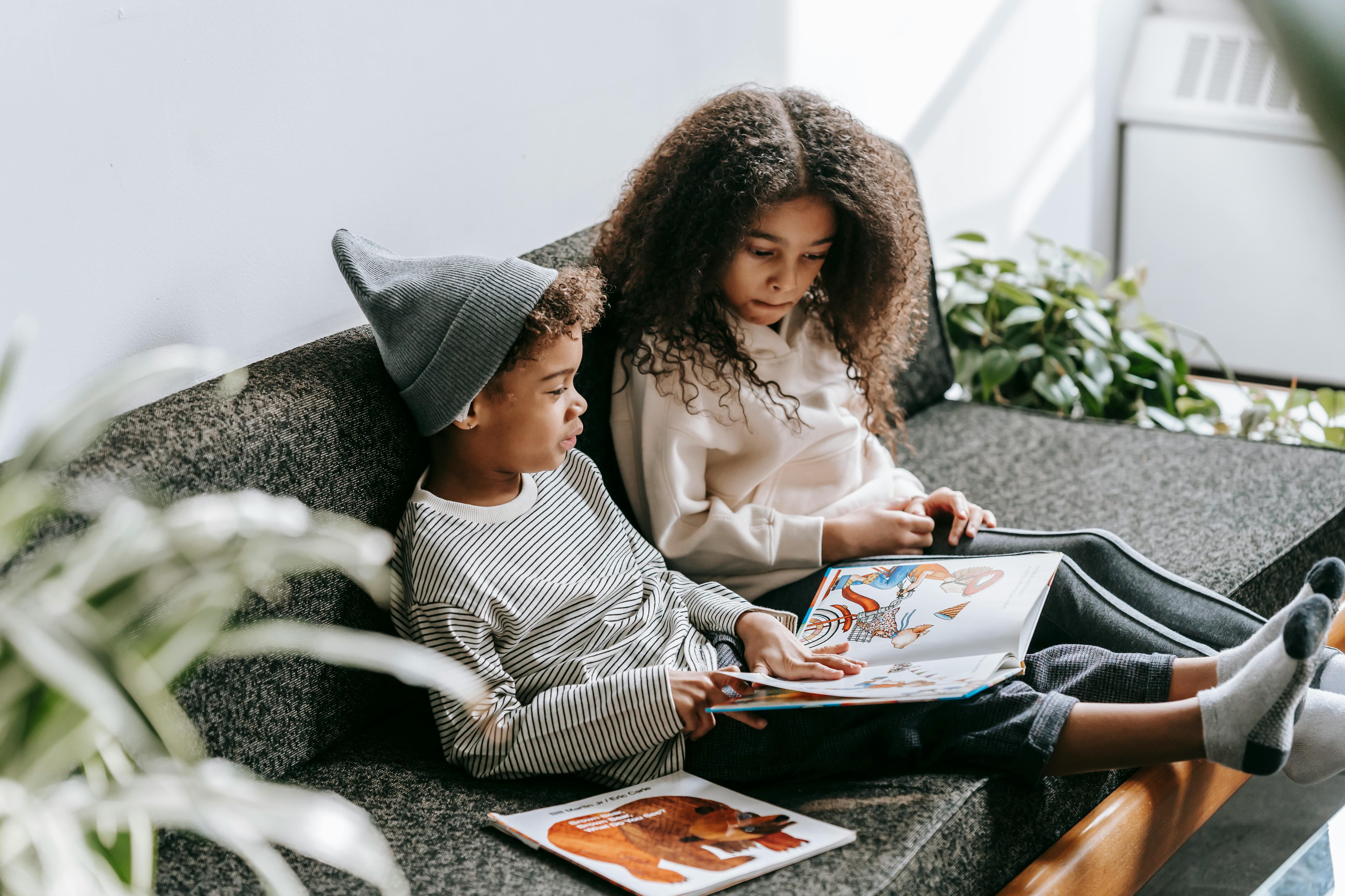 focused black children reading fairytale on sofa