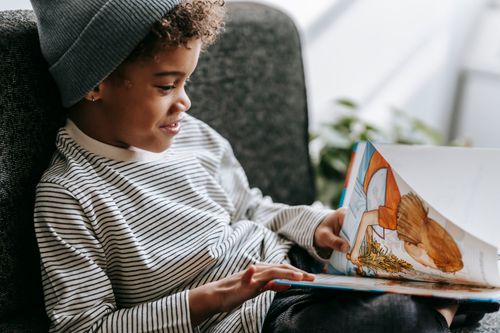 Free Side view of crop glad African American boy with curly hair smiling and watching pictures of book on blurred background Stock Photo