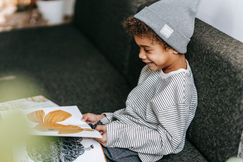 Free From above of adorable positive clever African American boy in stylish casual outfit flipping pages of book with colorful pictures Stock Photo