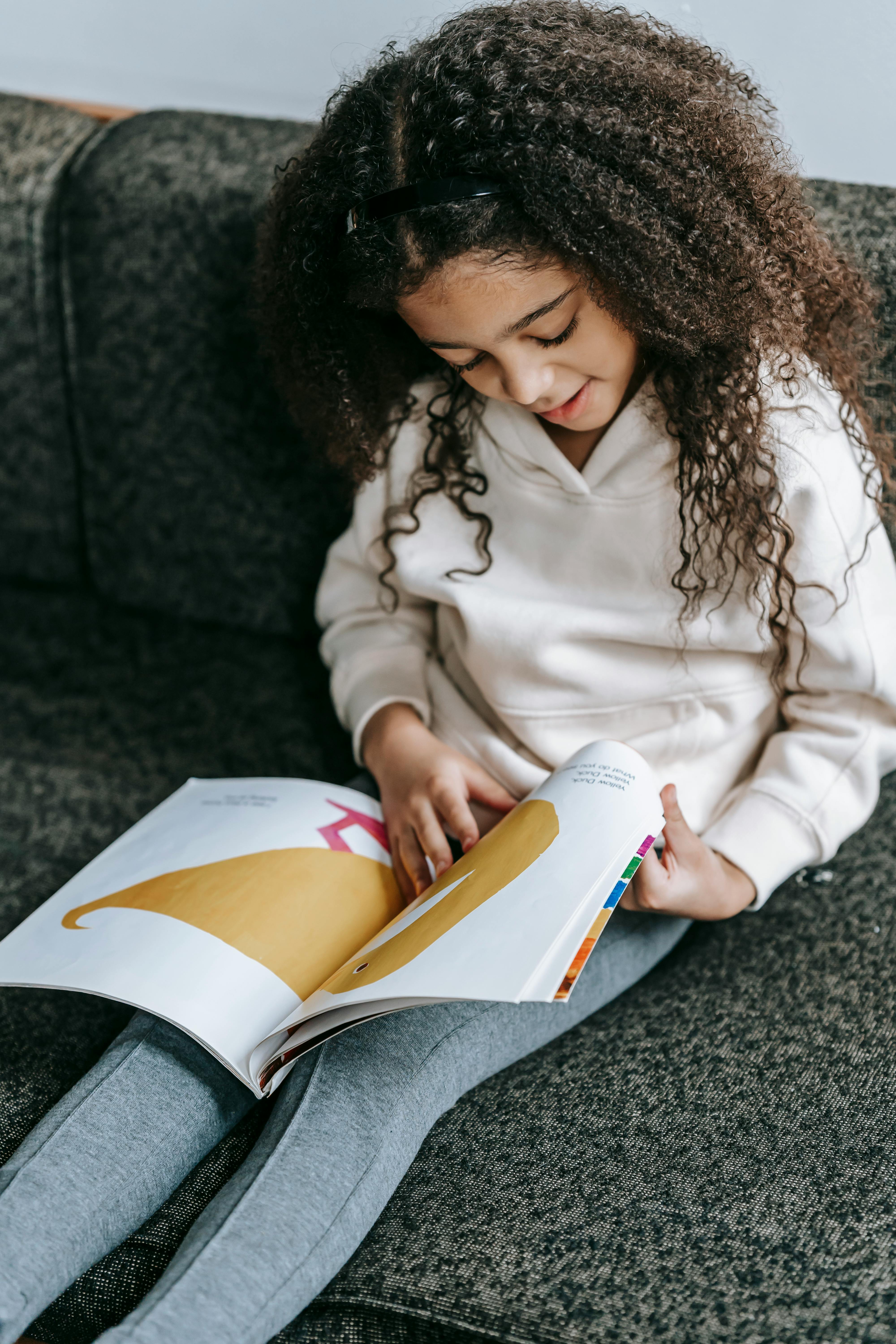 adorable black girl reading story with colorful pictures in book