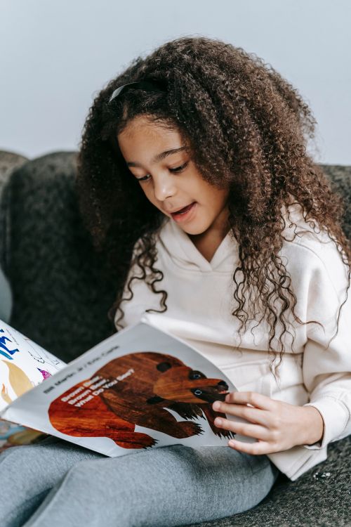 Free Cute clever African American girl with long curly hair learning reading book with bright illustrations of animals Stock Photo