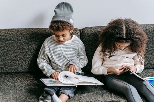 Free Smart adorable African American boy and girl flipping pages of interesting book on couch in daytime Stock Photo