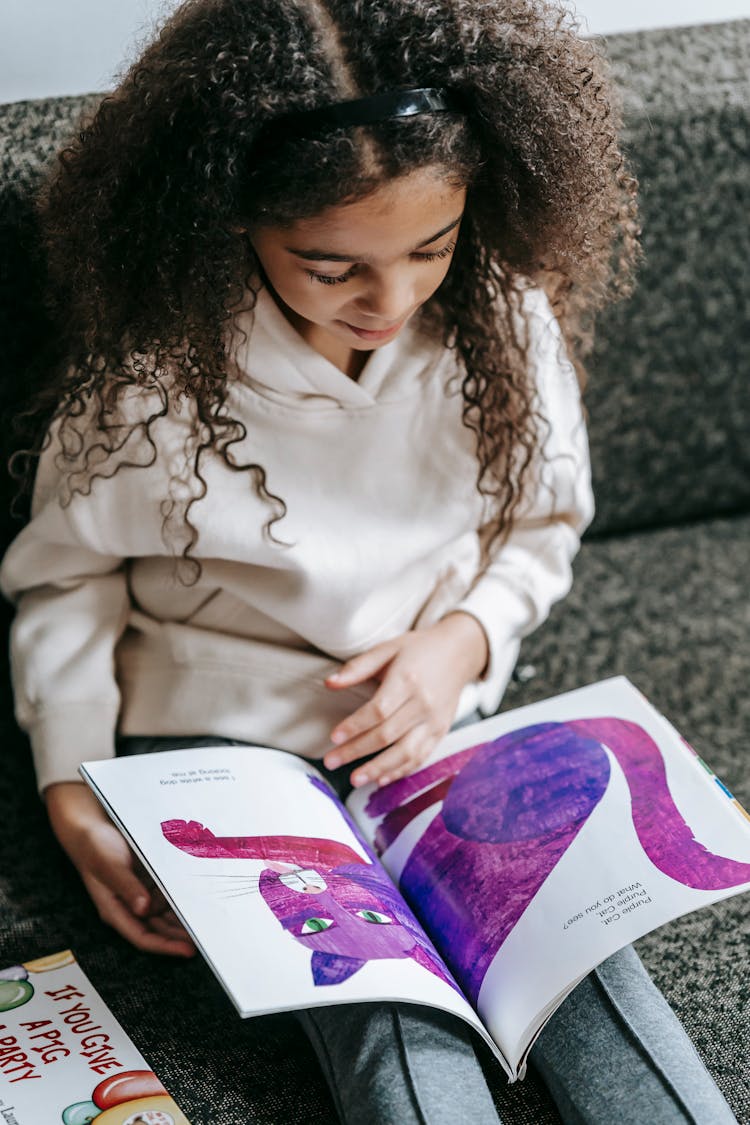 Black Girl Looking At Picture Of Purple Cat In Book