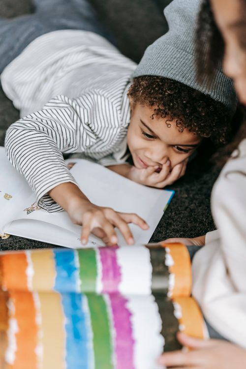 Free High angle of crop anonymous ethnic girl drawing in sketchbook sitting on sofa near cute little brother lying on couch Stock Photo